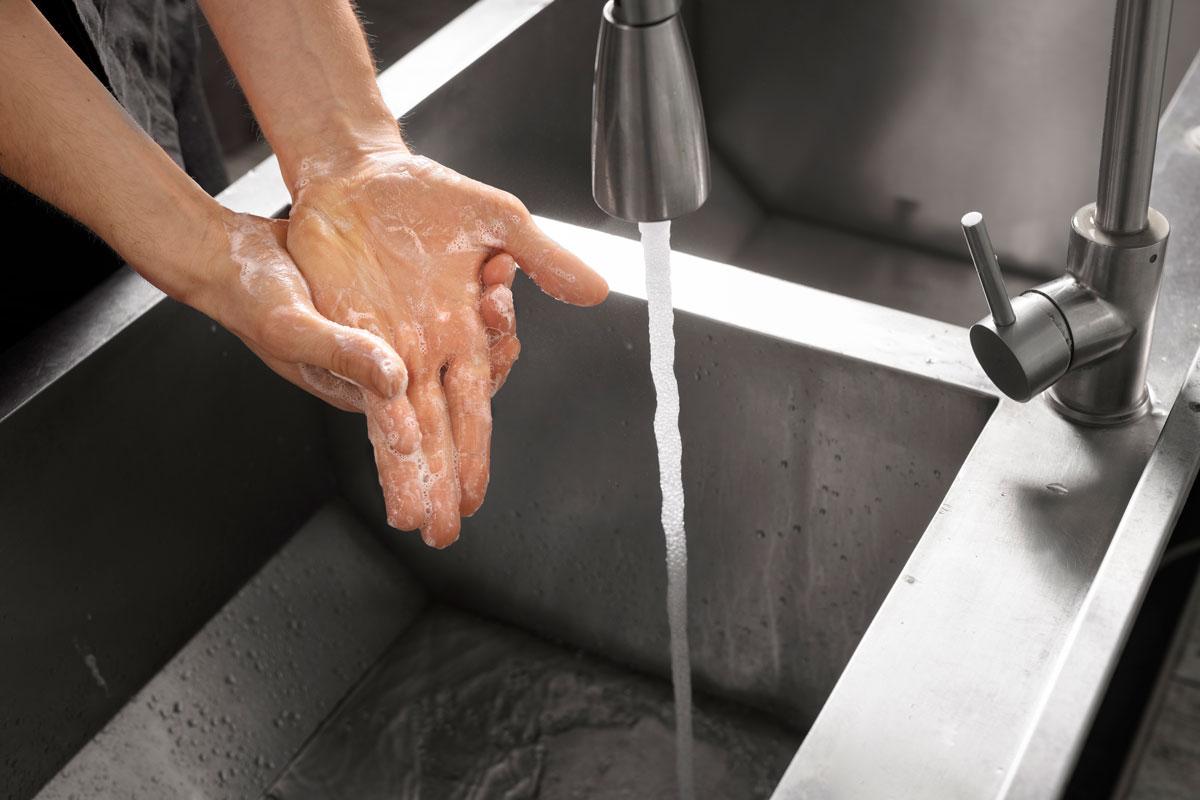 Jemand wäscht seine Hände mit Seife in einem großen Gastronomie-Waschbecken