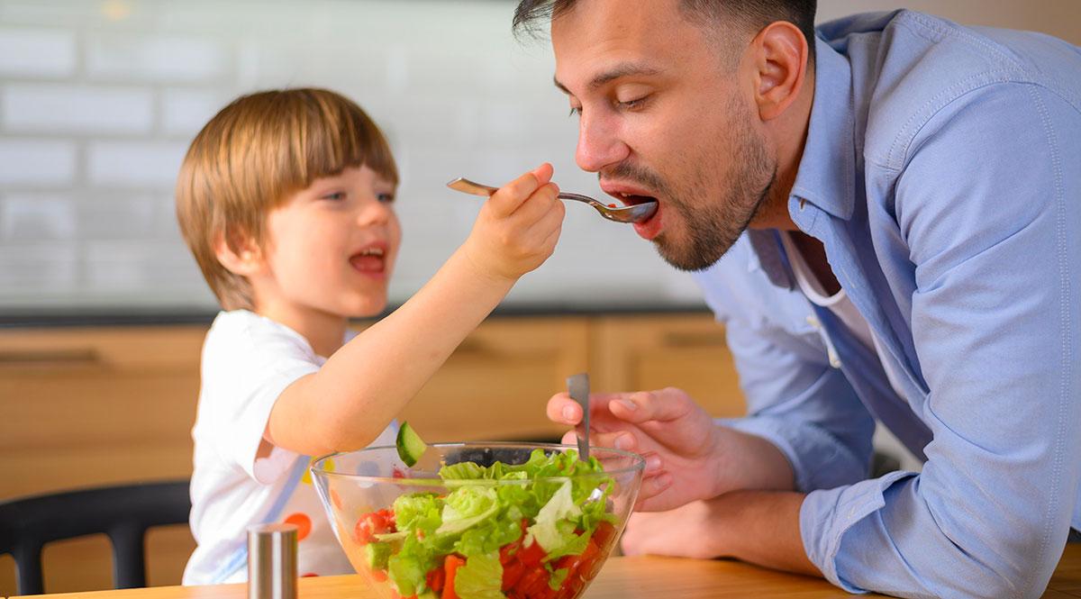 Ein Kind füttert einen erwachsenen Mann mit Salat