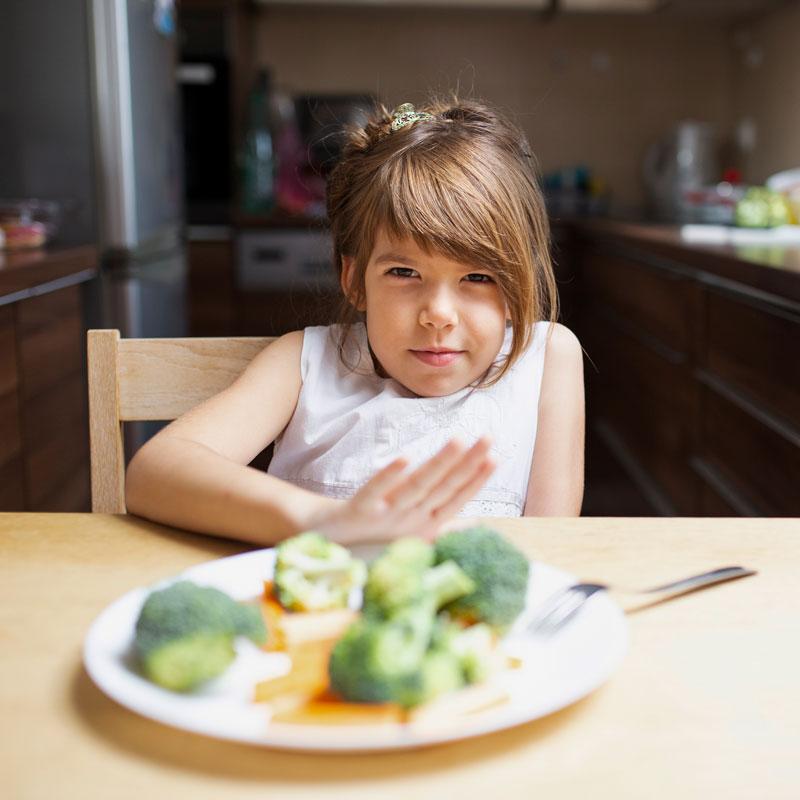 Ein Kind schiebt einen Teller mit Gemüse von sich weg