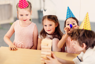 Drei Kinder mit bunten Papierhüten und ein Kind mit Krone sitzen an einem Tisch