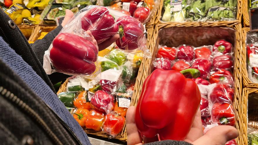 Im Supermarkt hält jemand unverpackte und in Plastikfolie verpackte rote Paprika in der Hand