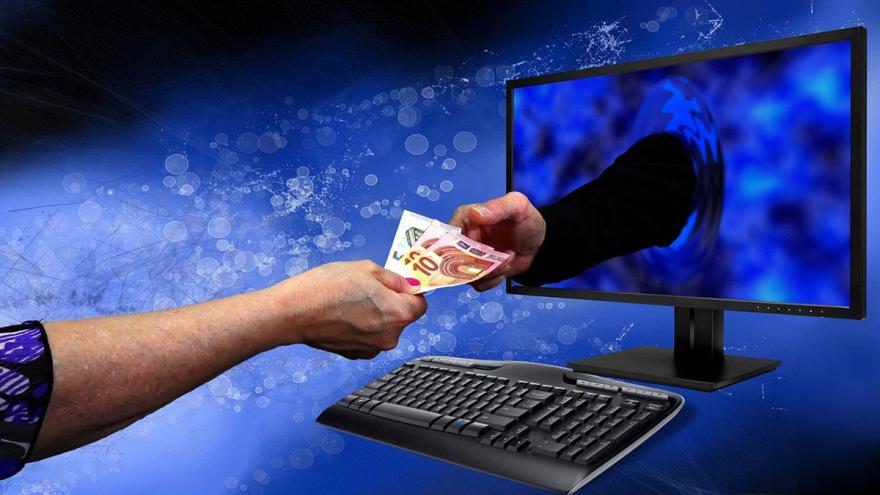 Eine Hand reicht Geldscheine zu einer anderen Hand, die aus einem Bildschirm kommt