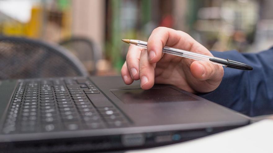 Eine Hand hält einen Kugelschreiber, darunter eine Laptop-Tastatur