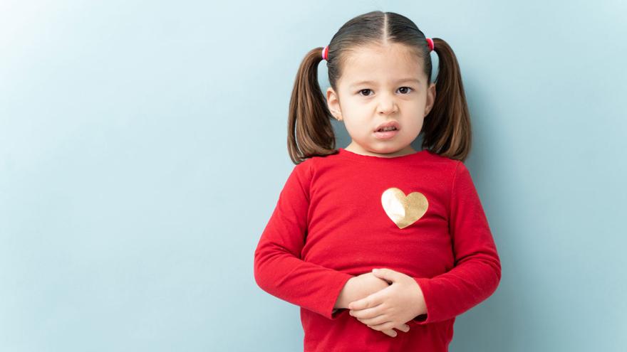 Ein kleines Mädchen im roten Shirt hält sich die Hände vor den schmerzenden Bauch