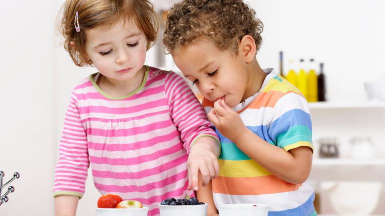 Kleines Mädchen und kleiner Junge essen verschiedene Obstsorten aus Schälchen